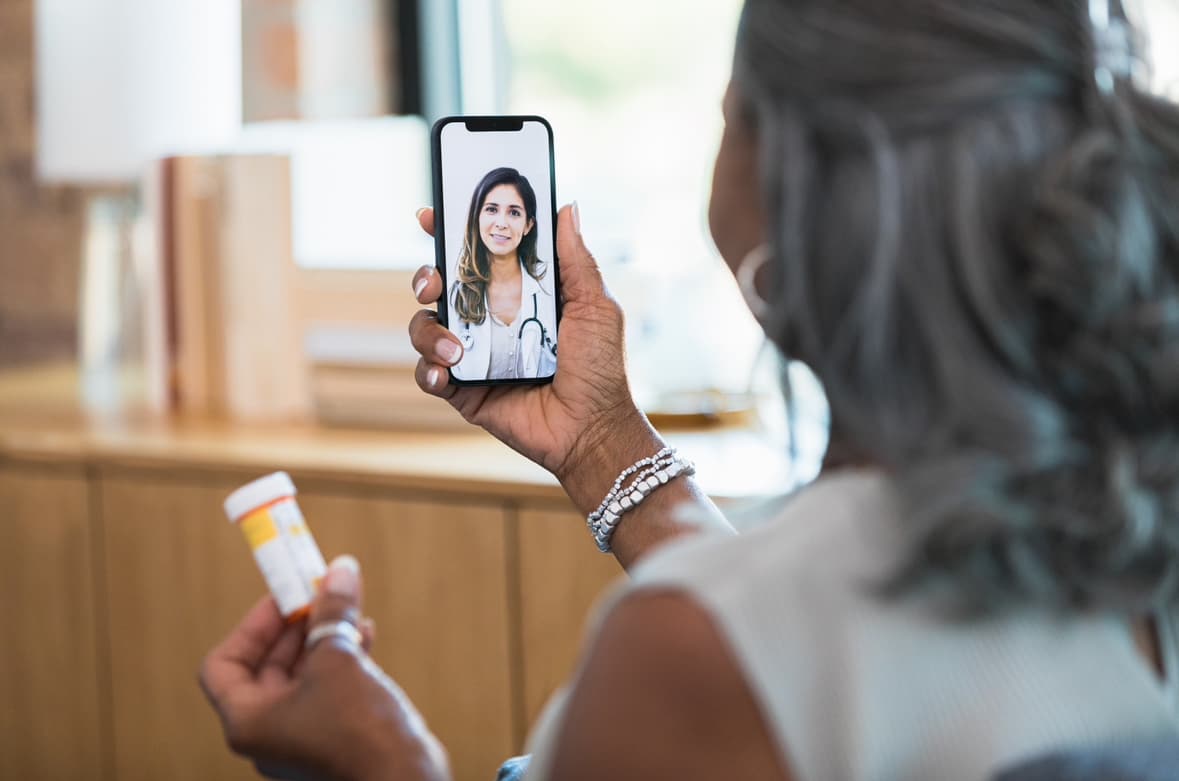 Senior woman having a virtual consultation with a female doctor on a smartphone while holding a prescription bottle, representing telemedicine and online medication management.